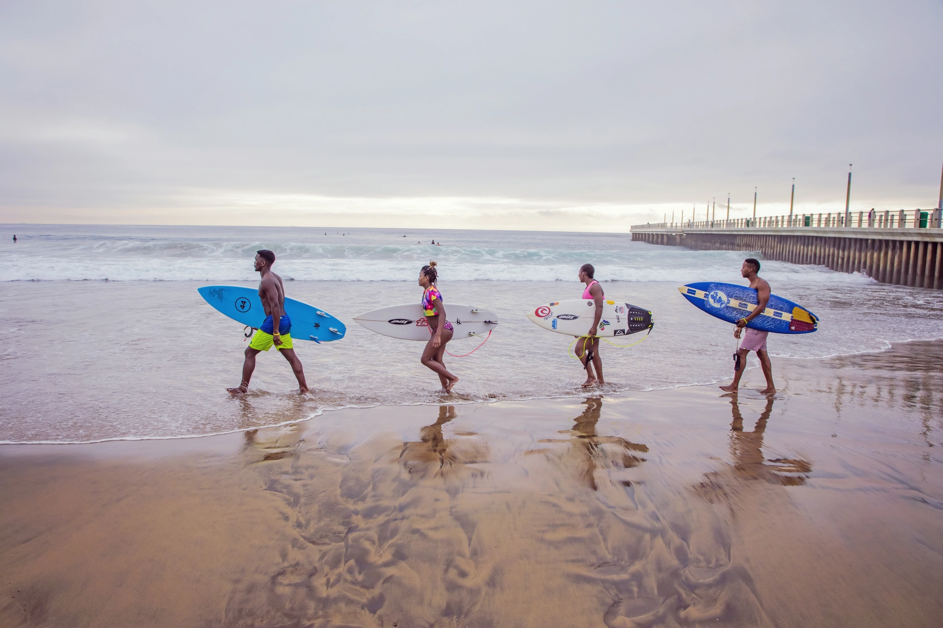 Four surfers carrying their surf boards on a beach
